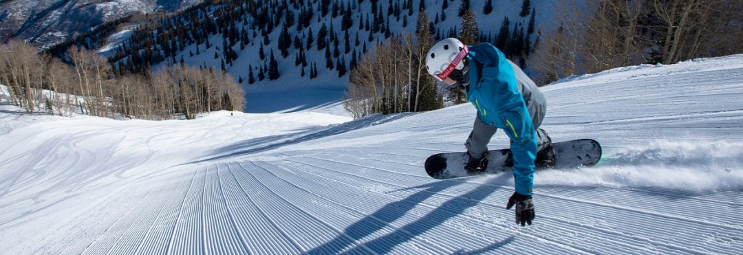 Chris Klug snowboarding down fresh corduroy on a steep snow covered groomed slope in the mountains at Aspen Mountain Ski Resort in Colorado